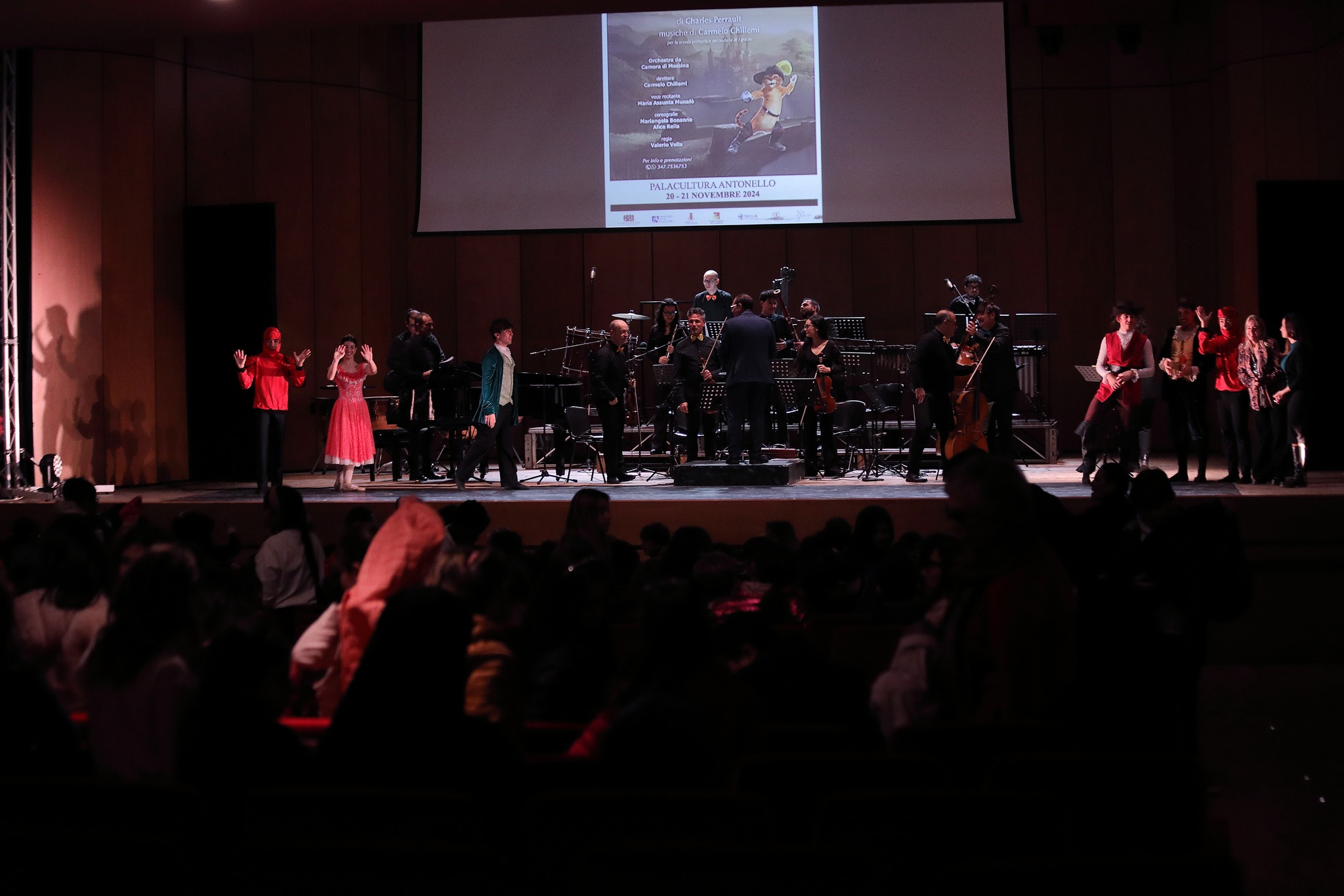 Vista dalla platea — tutto il cast e l'orchestra, locandina 2024 sullo schermo, Palacultura Antonello