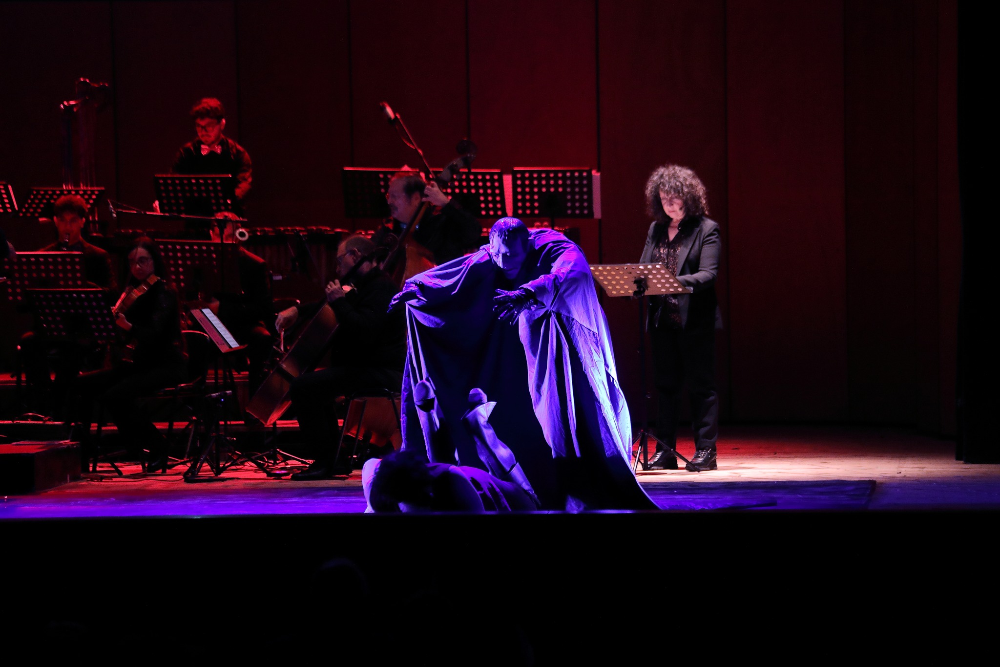 Scena con il mago trasformato — personaggio con mantello scuro e l'orchestra sullo sfondo